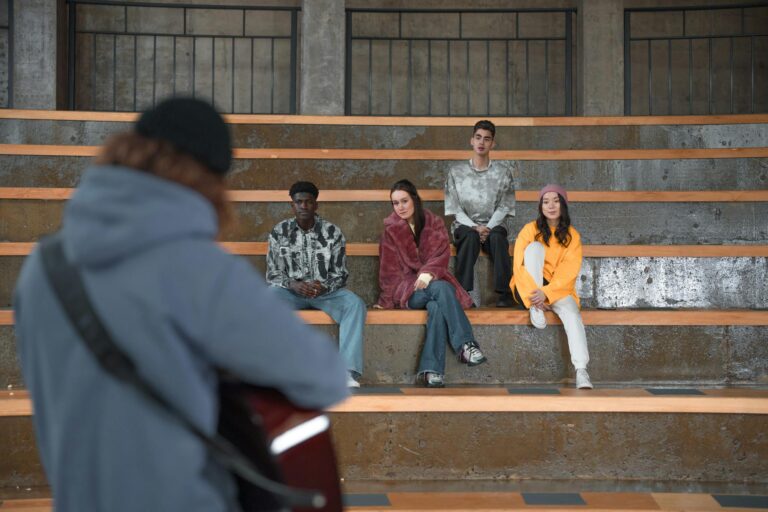 A diverse group of young adults attentively watching a guitar performance indoors.
