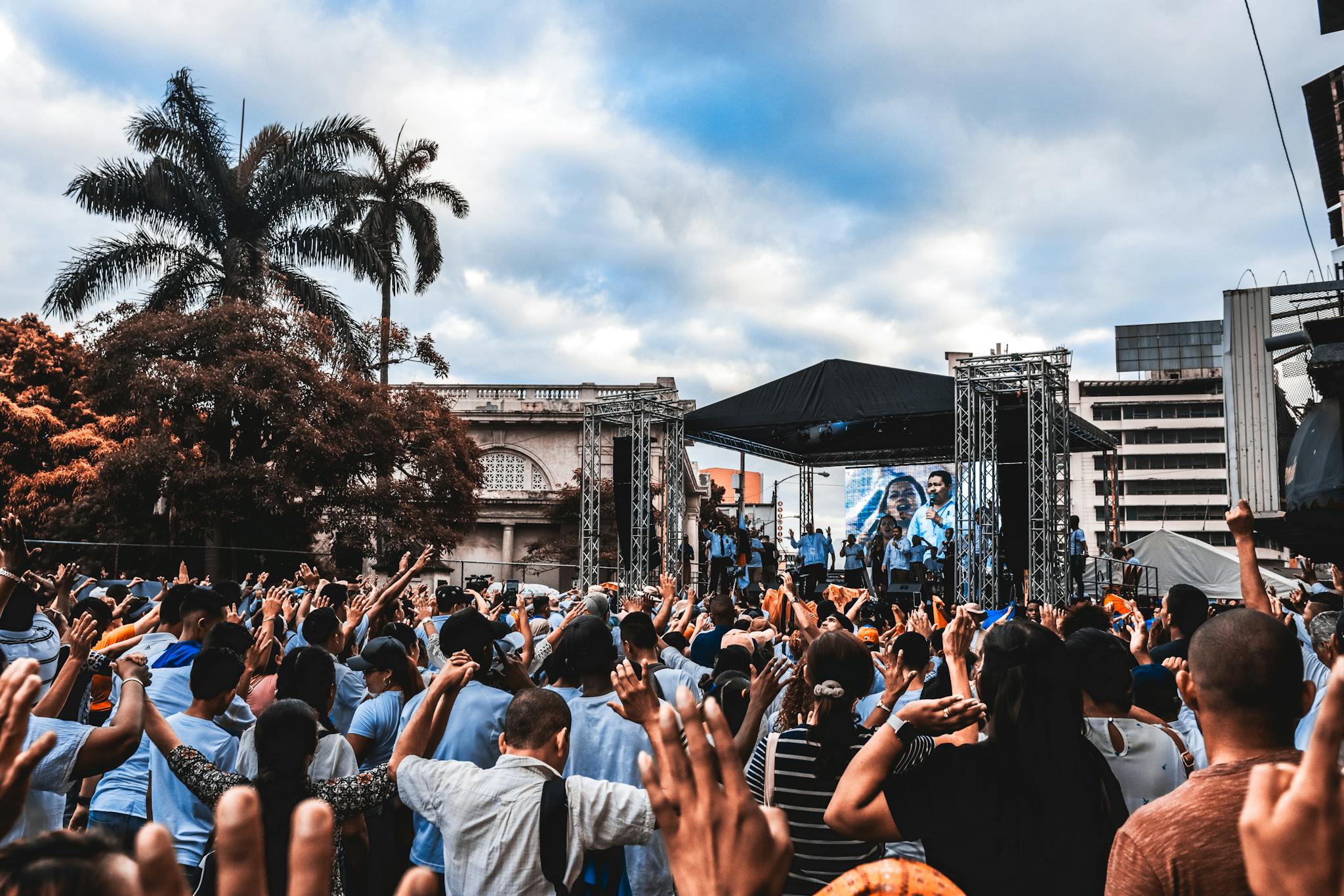 Dynamic scene at an outdoor concert with a large, enthusiastic crowd raising their hands.